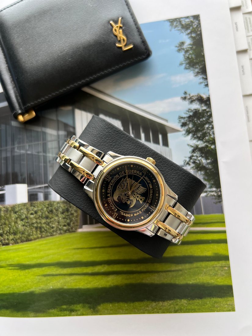 Reloj conmemorativo de acero y oro con la carátula negra de la Escuela Superior de Guerra y la leyenda «Saber más para servir».