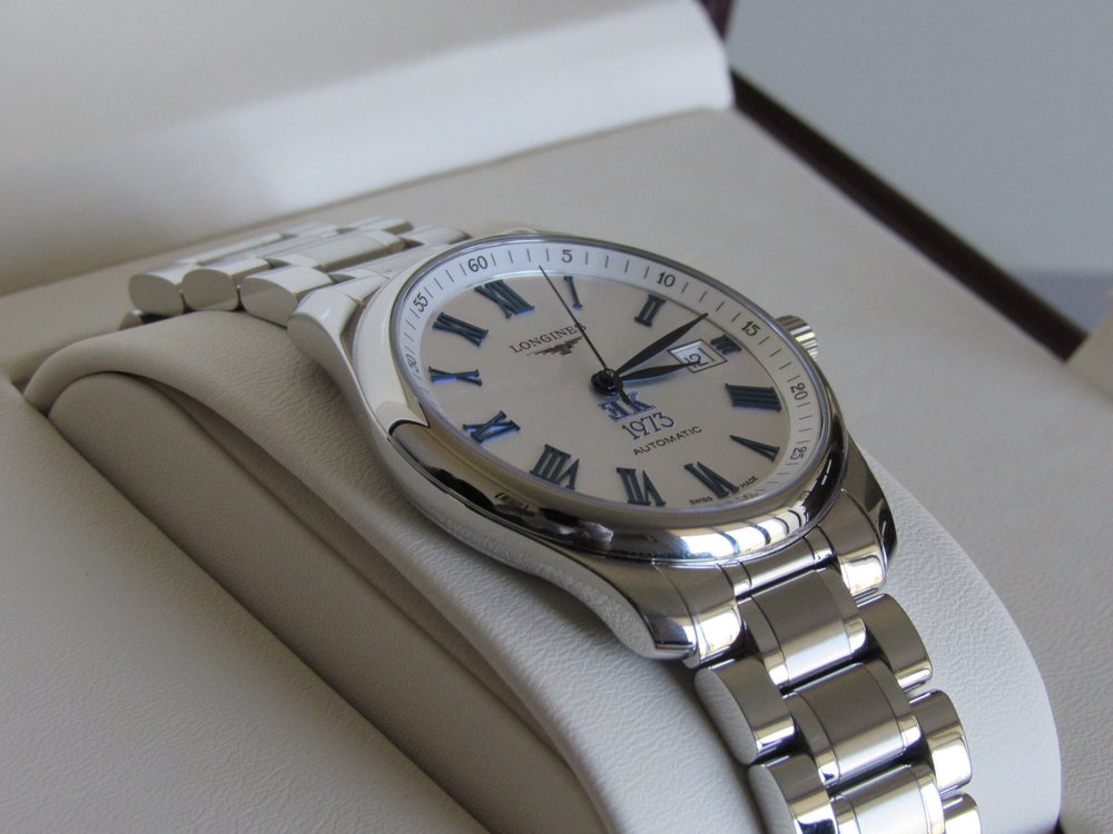 El reloj de tres cuartos sobre un cojín claro, con el brazalete extendido.