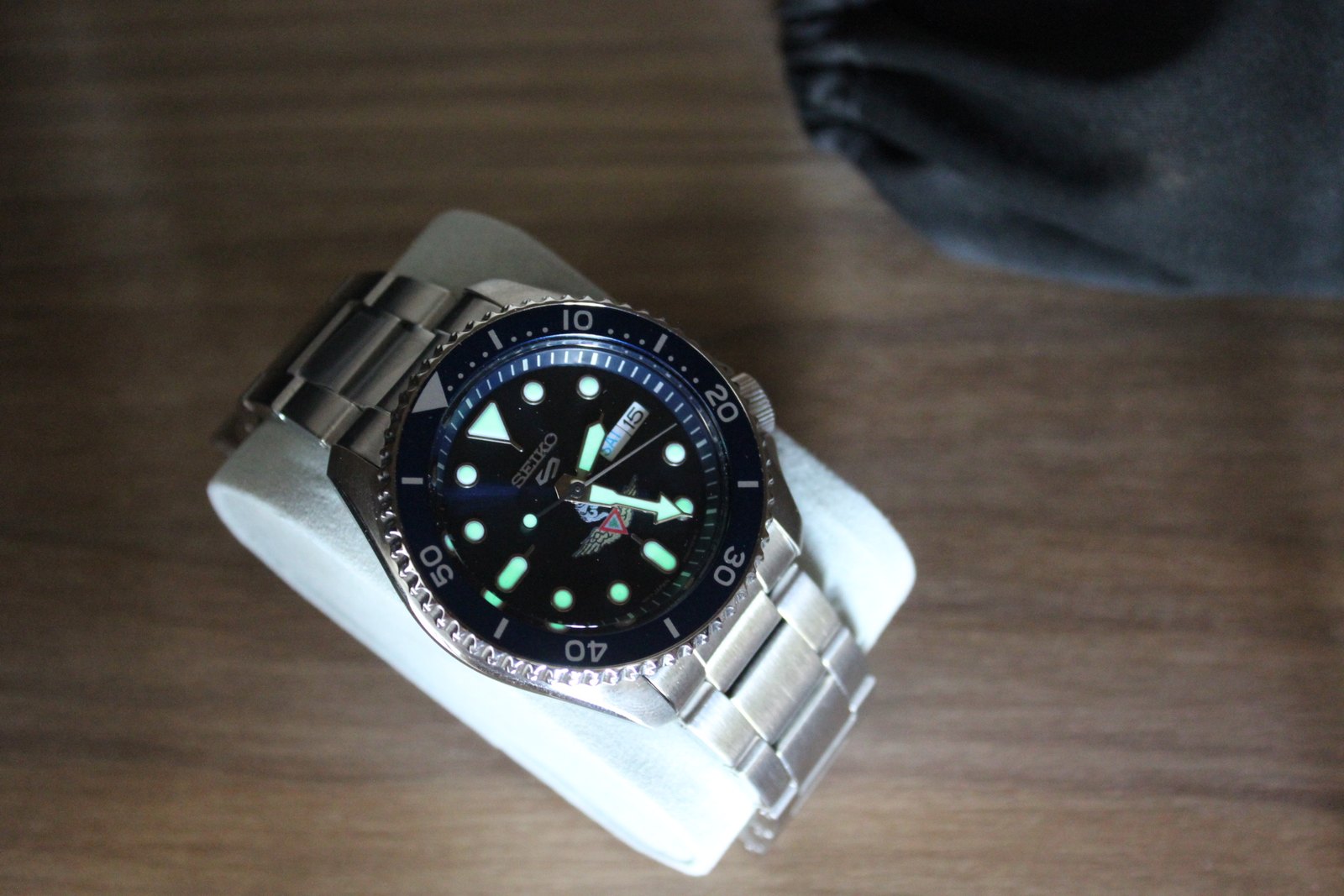 El reloj sobre una superficie de madera, con la esfera azul y el emblema alado a la vista.
