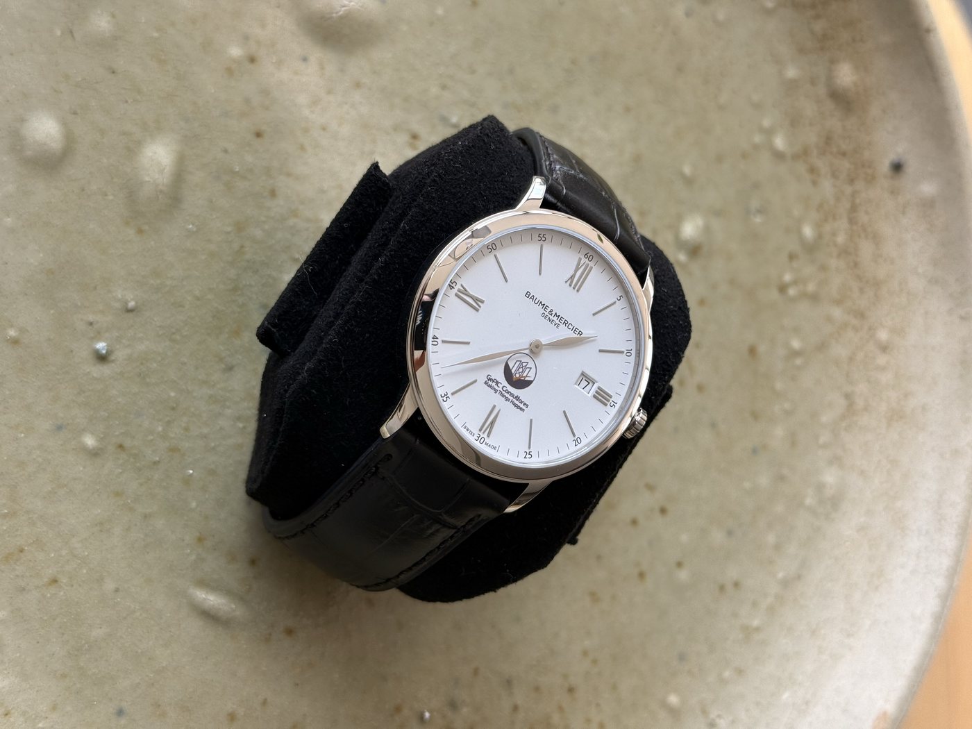 Reloj de carátula blanca y correa de piel negra, colocado dentro de su estuche.