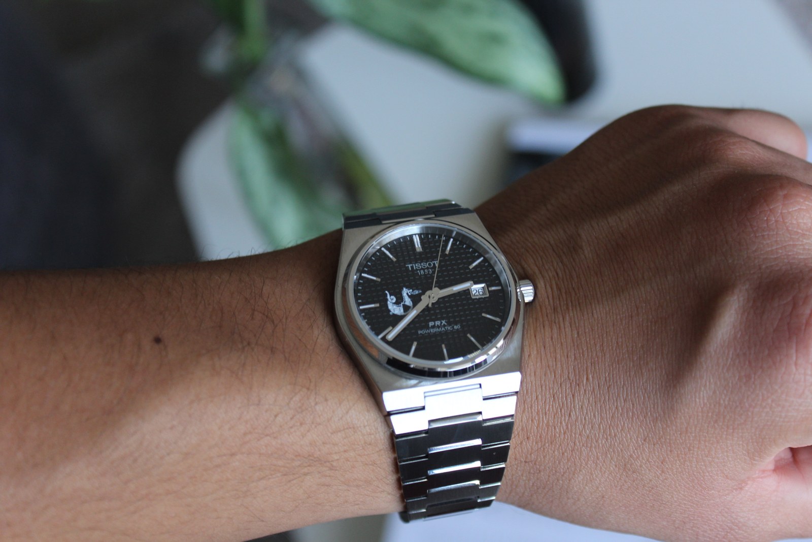 El reloj Tissot puesto en la muñeca, con la carátula negra de frente y el logotipo del cliente impreso en la esfera.